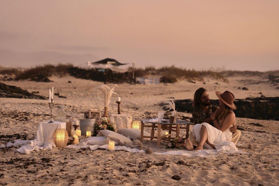 Strand Elopement Fuerteventura – Brautpaar am Holztisch mit Kerzen und Laternen, barfuß © Chirlyart